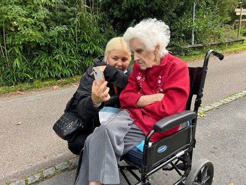 Carer outside with a client in a wheelchair, looking at a mobile phone